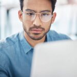 Homem com óculos concentrado em um laptop, relacionado à vaga de Home Office na Gupy.